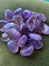 Load image into Gallery viewer, A Pile of Light Purple Ametrine Tumbles sitting atop a forest green felt with slight yellow inclusions