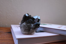 Load image into Gallery viewer, Multiple point Smokey Quartz cluster with raw base and grey-brown in colour, sitting atop a book