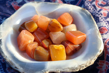 Load image into Gallery viewer, Handful of Red Aventurine Tumbles showing a wide variety of shades from a very light yellow, citrus orange and warm reds, held in a chalcedony bowl
