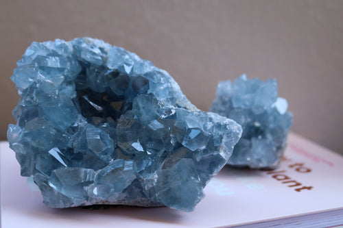 Two Celestite clusters with larger one in the forefront and small chunk in the background, both a pretty sea blue