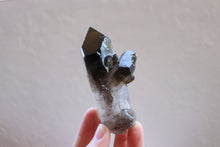 Load image into Gallery viewer, Two sided Smokey Quartz cluster with  raw base and grey-brown in colour, being held by fingertips
