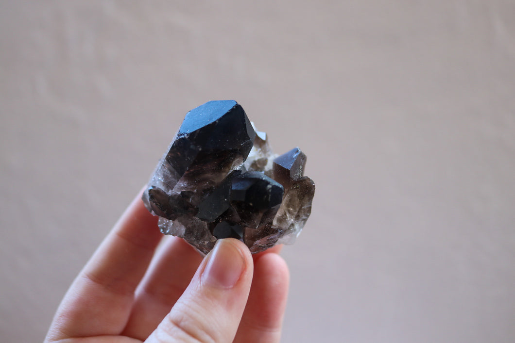 Chunky Smokey Quartz cluster with  raw base and grey-brown in colour, being held by fingertips