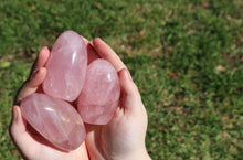 Load image into Gallery viewer, 3 Rose Quartz boulders being cupped in hands above grass.
