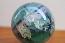 Load image into Gallery viewer, Close up of light coloured medium sized polished Fluorite sphere with Purple, Pink, Green and aqua inclusions
