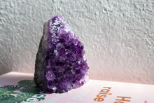 Load image into Gallery viewer, Medium sized triangular amethyst cluster sitting atop a book, combined deep purple, facing towards light source
