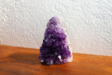 Load image into Gallery viewer, Medium sized triangular amethyst cluster sitting atop orange coloured bench, combined dark purple to lilac 
