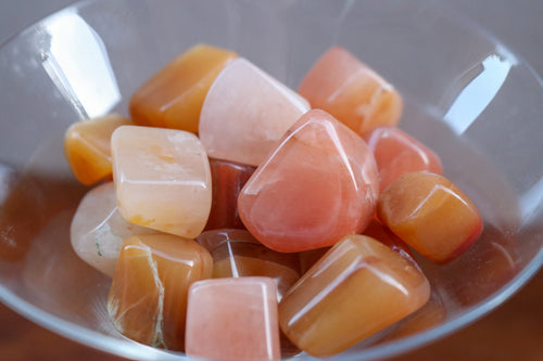Handful of Red Aventurine Tumbles in a wide variety of shades from a very light yellow, peachy pink, citrus orange and warm reds, held in a clear martini glass 