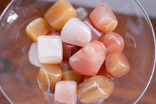 Load image into Gallery viewer, Birds eye view - Handful of Red Aventurine Tumbles in a wide variety of shades from a very light yellow, peachy pink, citrus orange and warm reds, held in a clear martini glass 
